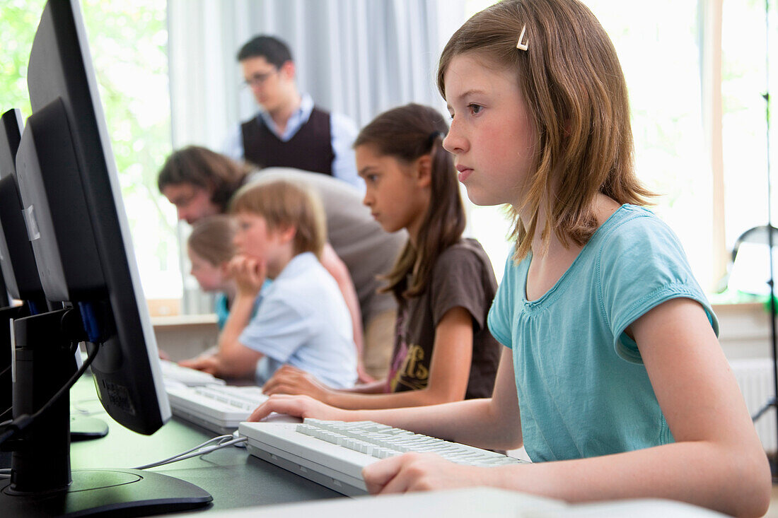 Male teachers helping pupils in computer room, Hamburg, Germany