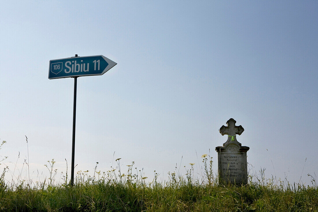 Road sign and wayside cross under clear sky, Sibiu, Transylvania, Romania, Europe