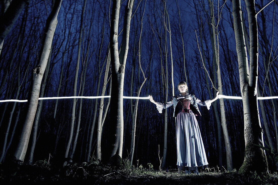 Young woman wearing a dirndl, traditional costume, standing in a forest at twilight, Kaufbeuren, Bavaria, Germany