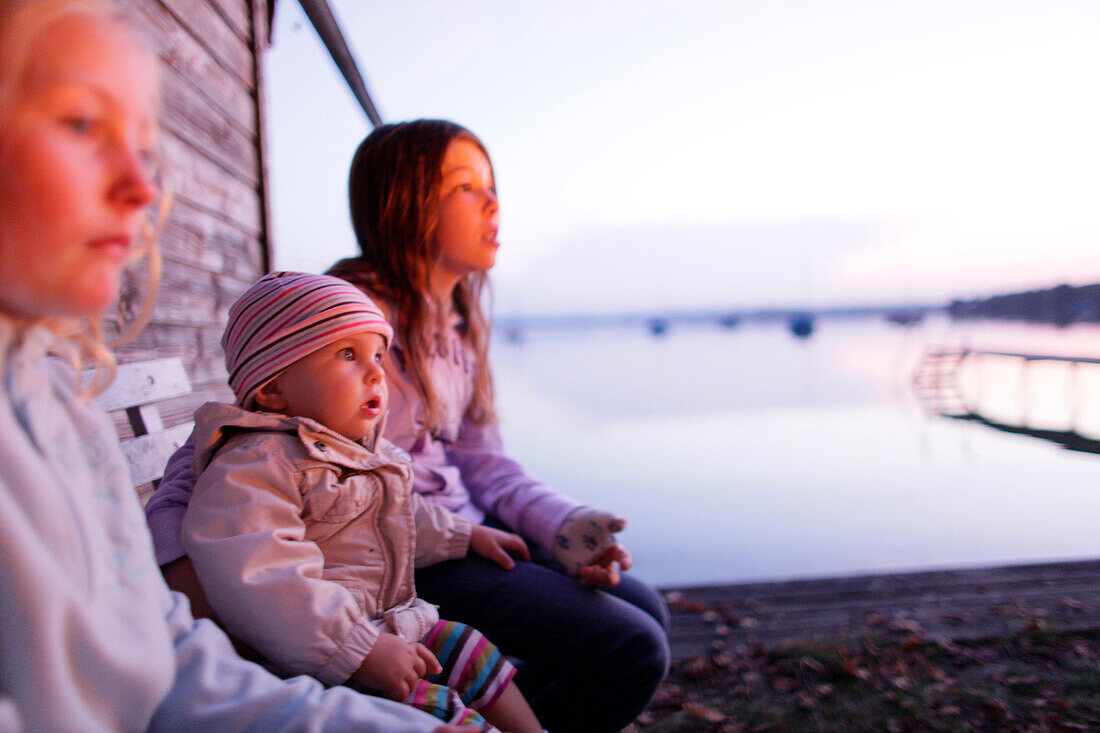 Children sitting beside hut at lake Worthsee, Bavaria Germany