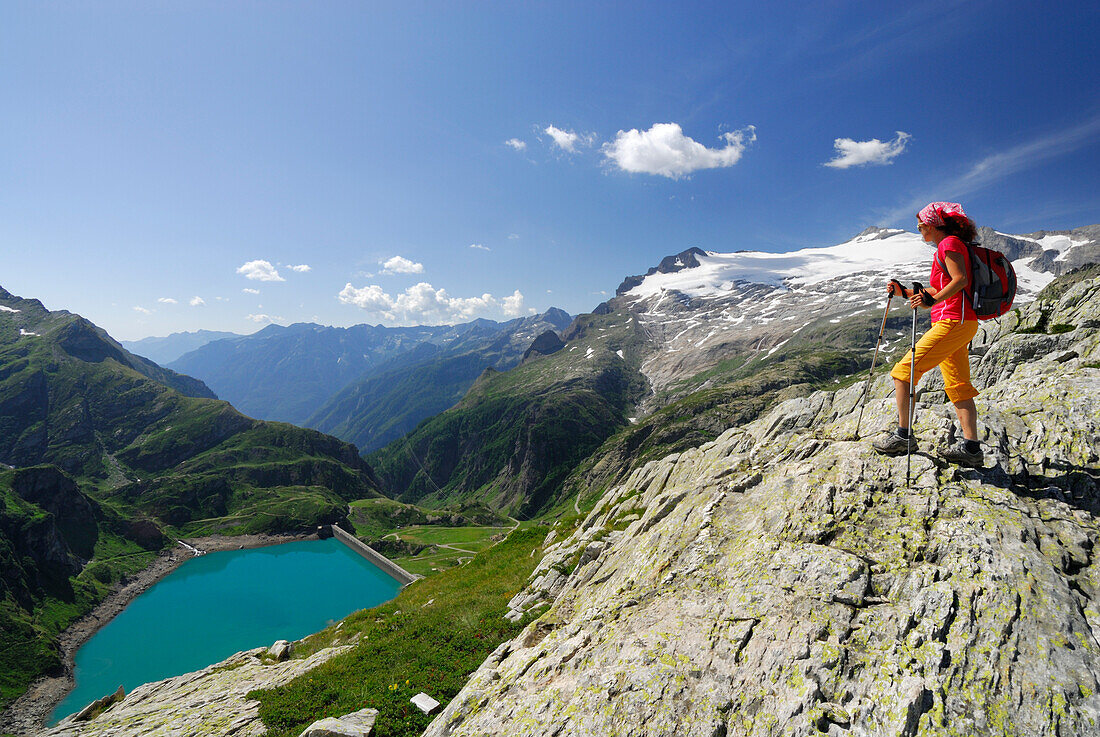 Female hiker looking over reservoir Lago di Robiei, Basodino glacier in background, Ticino Alps, Ticino, Switzerland