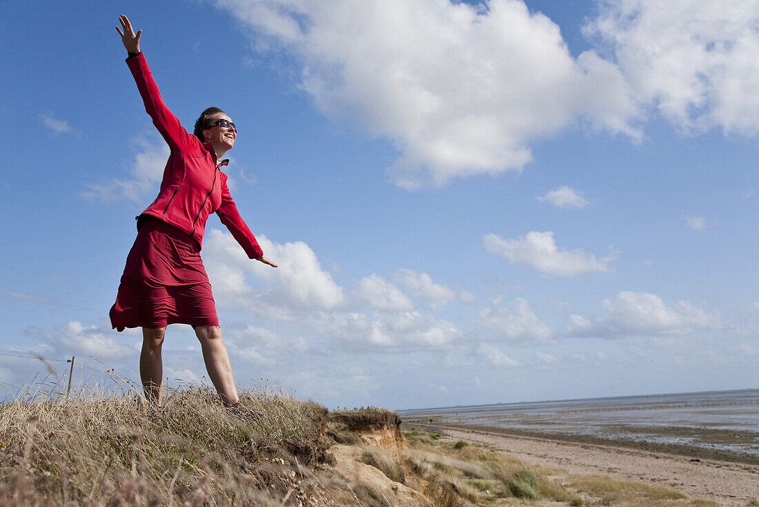 Frau mit ausgebreiteten Armen am Strand von Utersum, Insel Föhr, Schleswig-Holstein, Deutschland