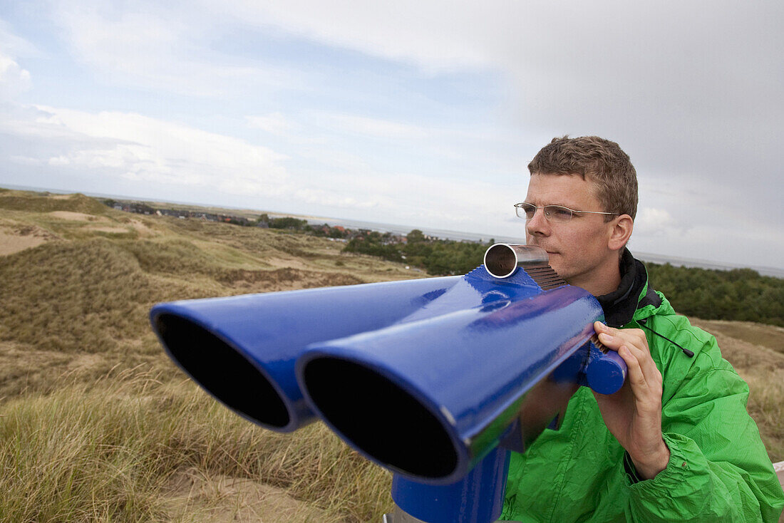 Man looking through coin-operated binoculars over dunes, Norddorf, Amrum island, Schleswig-Holstein, Germany