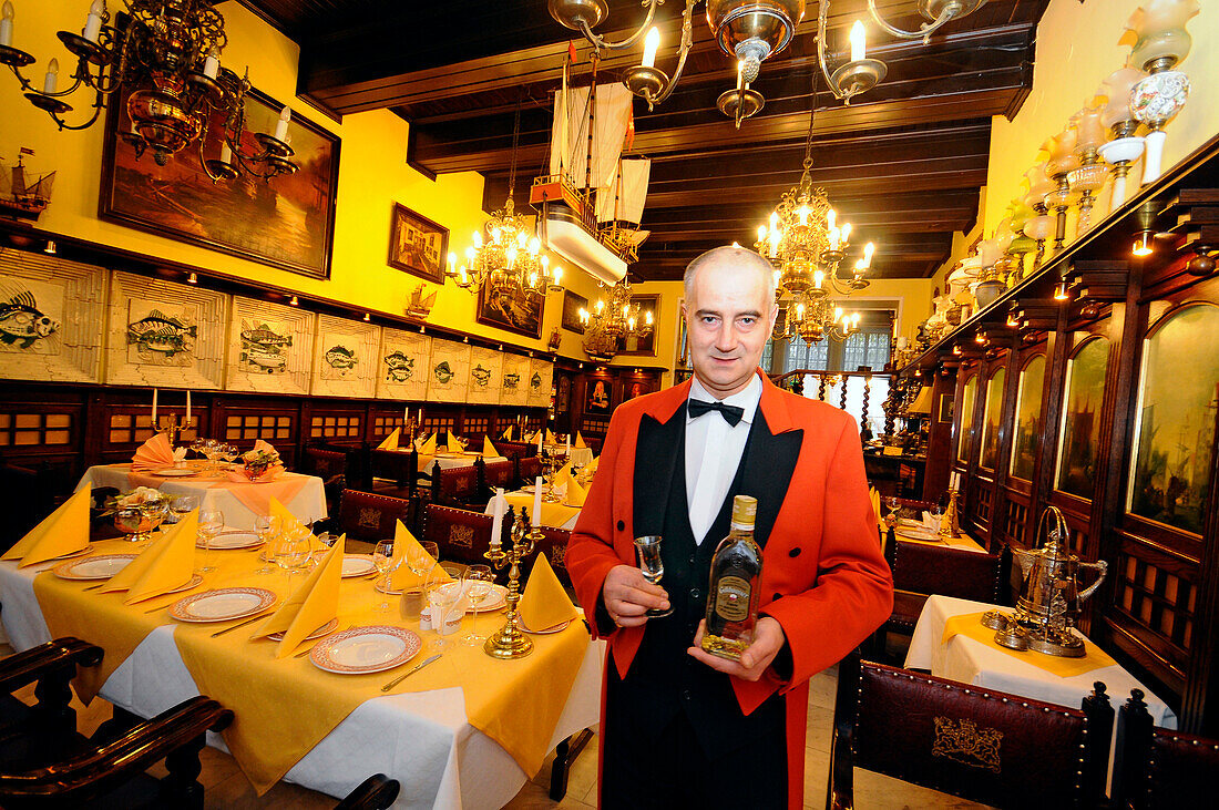 Waiter at the restaurant Pod Lososiem holding a bottle of gold water, Gdansk, Poland, Europe