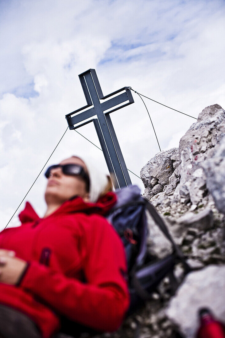 Woman resting beside summit cross, mountain Sonntagkarspitze, Innsbruck, Karwendel range, Tyrol, Austria