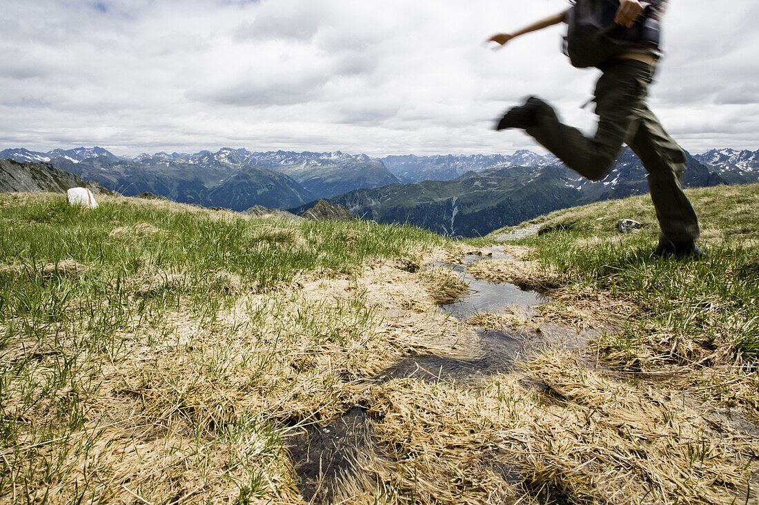 Frau springt über einen Bach, Sarotla Joch, Montafon, Vorarlberg, Österreich
