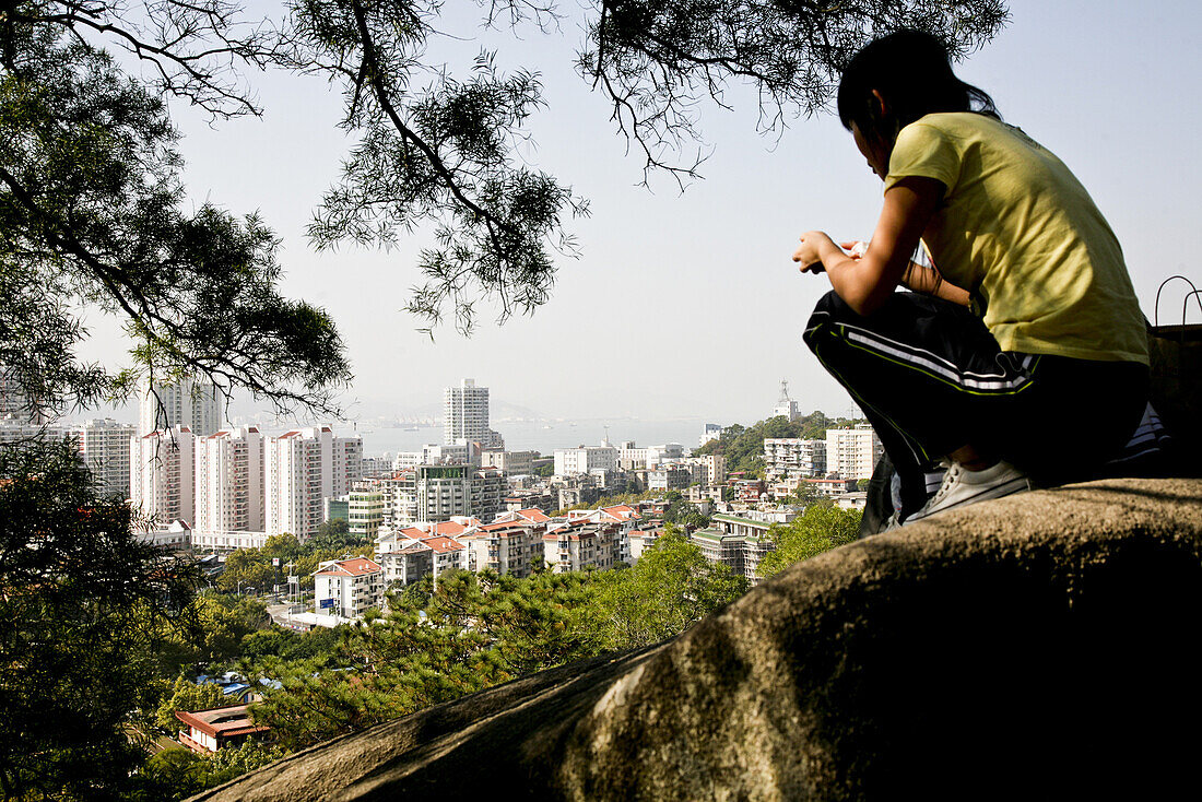 Junge Frau auf einem Felsen mit Blick über die Stadt, Stadtteil Siming, Xiamen, Fujian Provinz, China, Asien