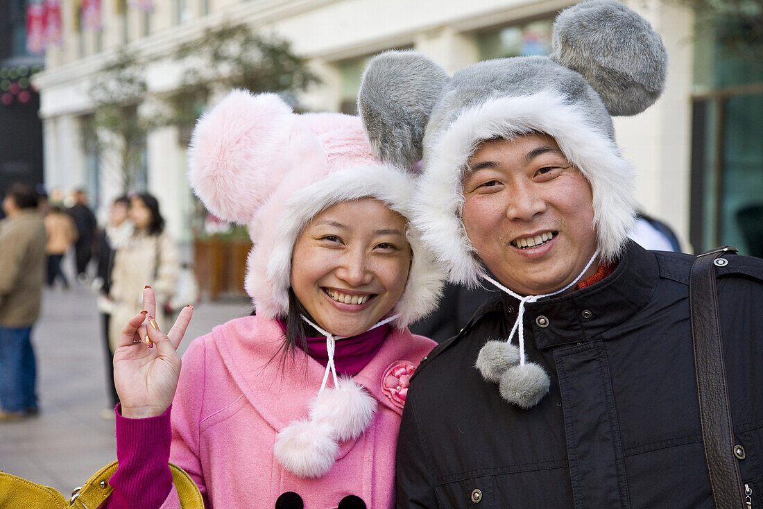 Chinesisches Paar mit lustigen Wintermützen in der Einkaufsstrasse Nanjing Lu, Shanghai, China, Asien