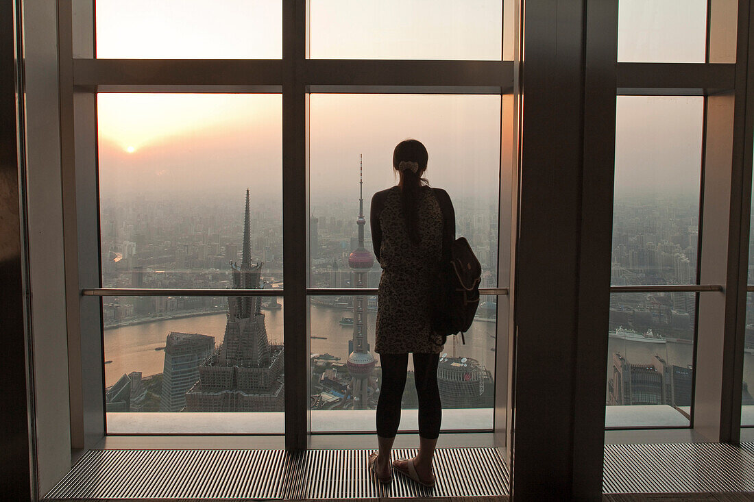 Frau blickt von der Aussichtsterrasse des World Trade Financial Center auf City von Shanghai und  Huangpu Fluss bei Sonnenuntergang, Pudong, Shanghai, China, Asien