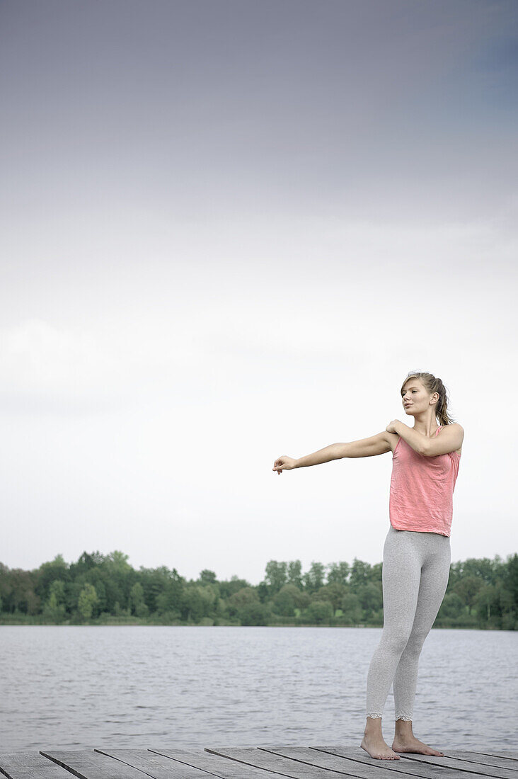 Junge Frau beim Stretching auf einem Steg am Starnberger See, Bayern, Deutschland