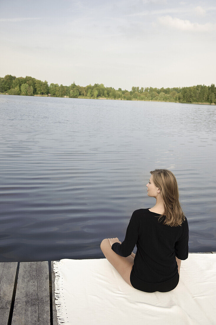 Junge Frau sitzt auf einem Steg am Starnberger See, Bayern, Deutschland