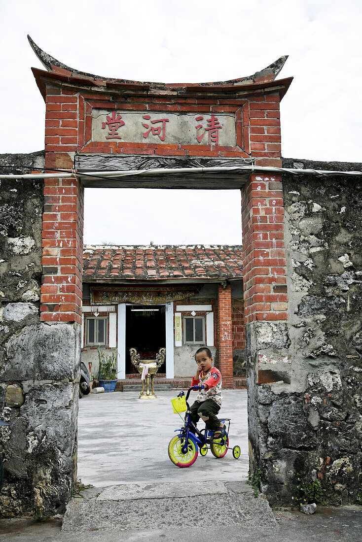 Junge auf Dreirad an traditionellem Eingangstor eines chinesischen Hauses, Qinghetang, Kenting, Republik China, Taiwan, Asien