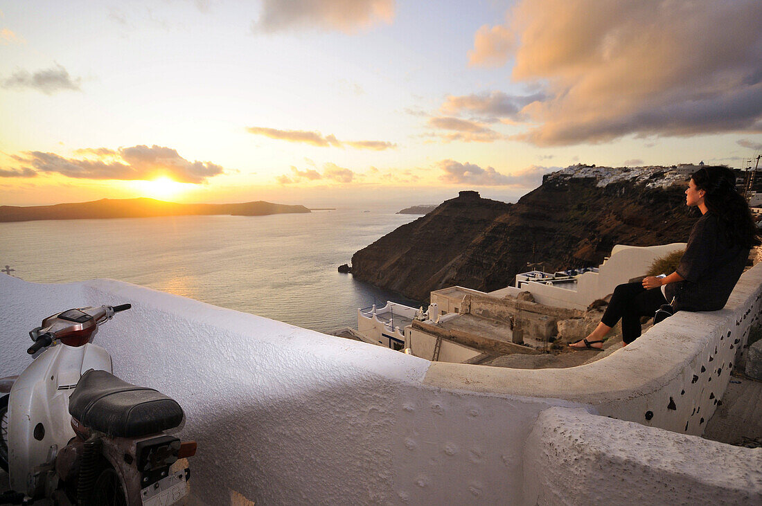 Frau auf einer Mauer betrachtet den Sonnenuntergang, Firostefani an der Caldera, Santorin, Kykladen, Griechenland, Europa