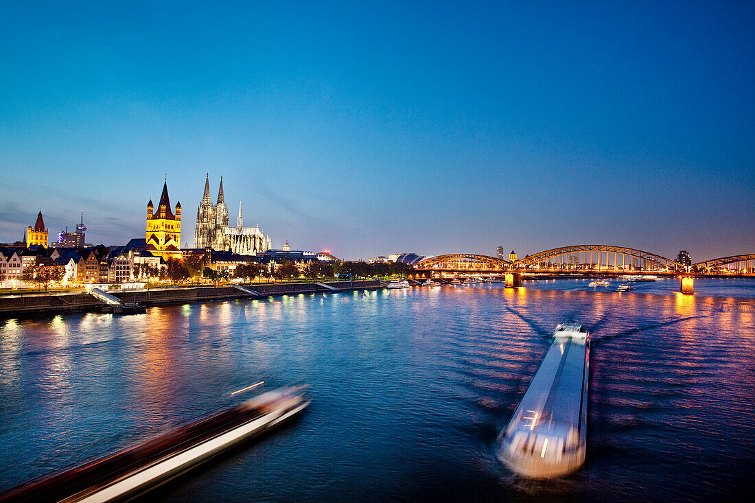 View over river Rhine to old town with cathedral and Great St. Martin church at night, Cologne, North Rhine-Westphalia, Germany