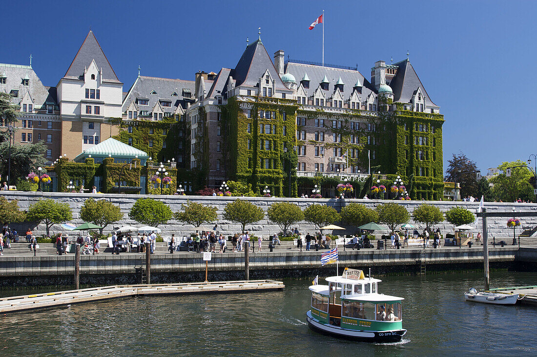 A view of Victoria,  British Columbia´s inner harbour,  showing the ivy covered Empress Hotel,  a small harbour ferry,  and tourists enjoying the sights and events along the inner harbour´s walk way