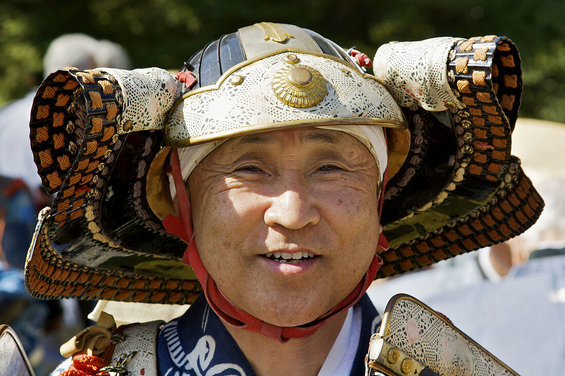 A head shot of a smiling Japanese man dressed up as a samurai for the Jidai Matsuri Festival of Ages in Kyoto,  showing showing helmet and head gear