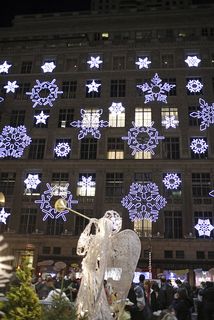 One of the famous Christmas angels of the Rockefeller Center made of wire with trumpet with Saks Fifth Avenue department store in the background which has been decorated with snow flakes designed by Svarovski, Manhattan,  New York City,  North America