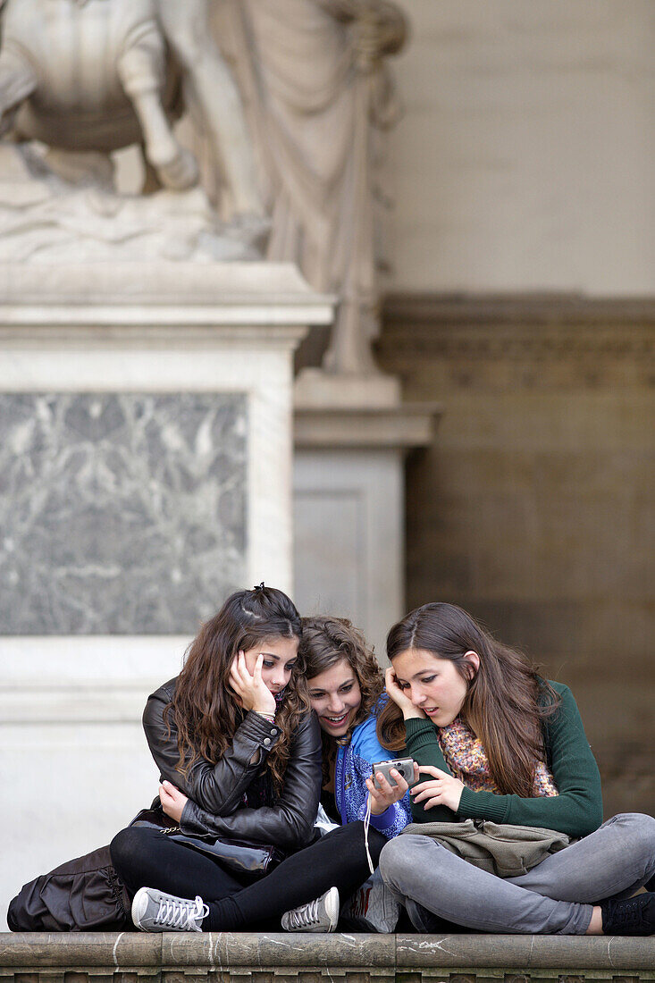 Three young girls sitting together at the Loggia dei Lanzi and looking at images of their digital camera,  Florence (Firence),  Tuscany,  Italy,  Southern Europe