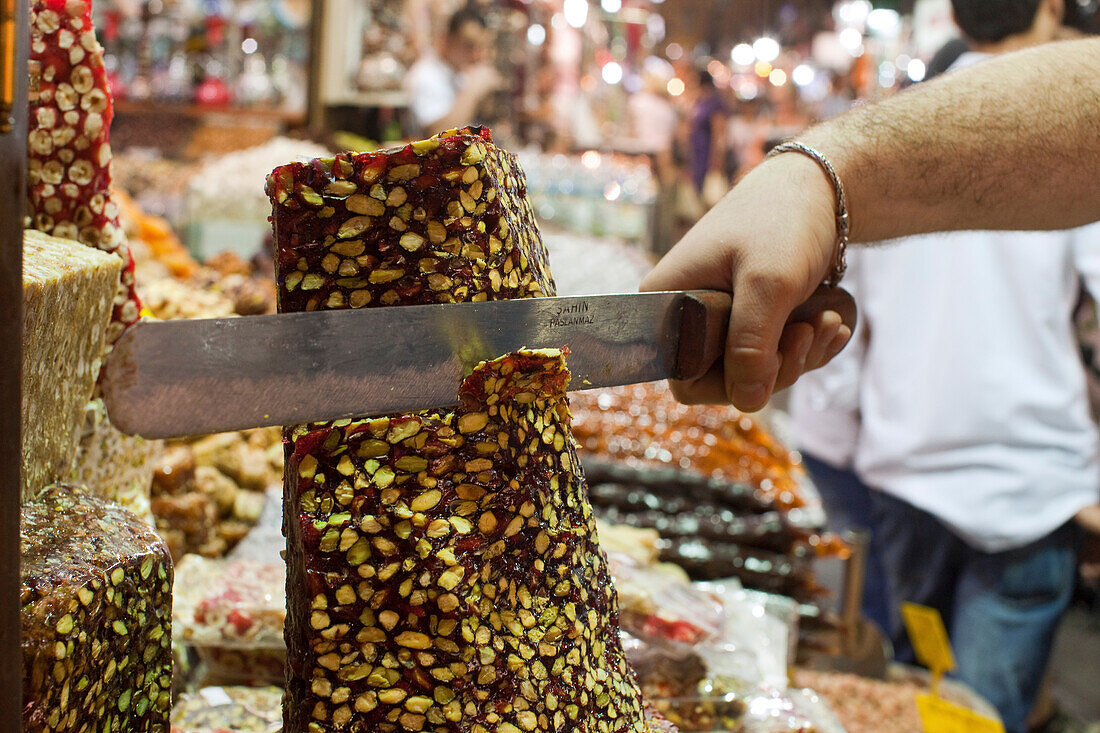 Süßigkeiten, Verkauf, mit einem großen Messer wird ein Stück von der Turmform abgeschnitten, Türkischer Honig, Halva mit Pistazien, Istanbul