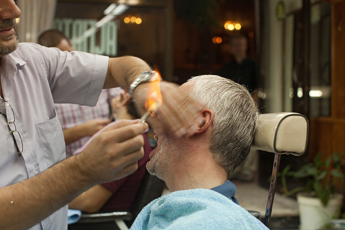 tourist at traditional barber, har removal, with cigarette lighter, Istanbul, Turkey