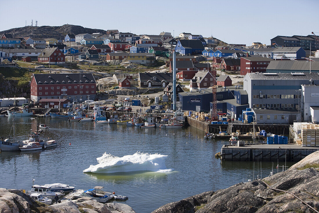 Iceberg at harbour with fishing boats and Royal Greenland Seafood Processing Plant, Ilulissat (Jakobshavn), Disko Bay, Kitaa, Greenland