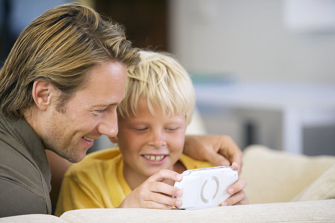 Addiction, Addictions, Adult, Adults, At home, Blond, Blonds, boy, boys, Caucasian, Caucasians, child, children, Color, Colour, Contemporary, Couch, Couches, Craving, dad, Fair-haired, families, family, father, fathers, grin, grinning, Handheld console, H