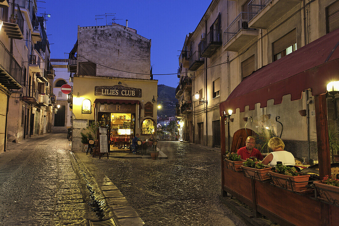 Gäste sitzen vor einem Restaurant am Abend, Cefalu, Sizilien, Italien