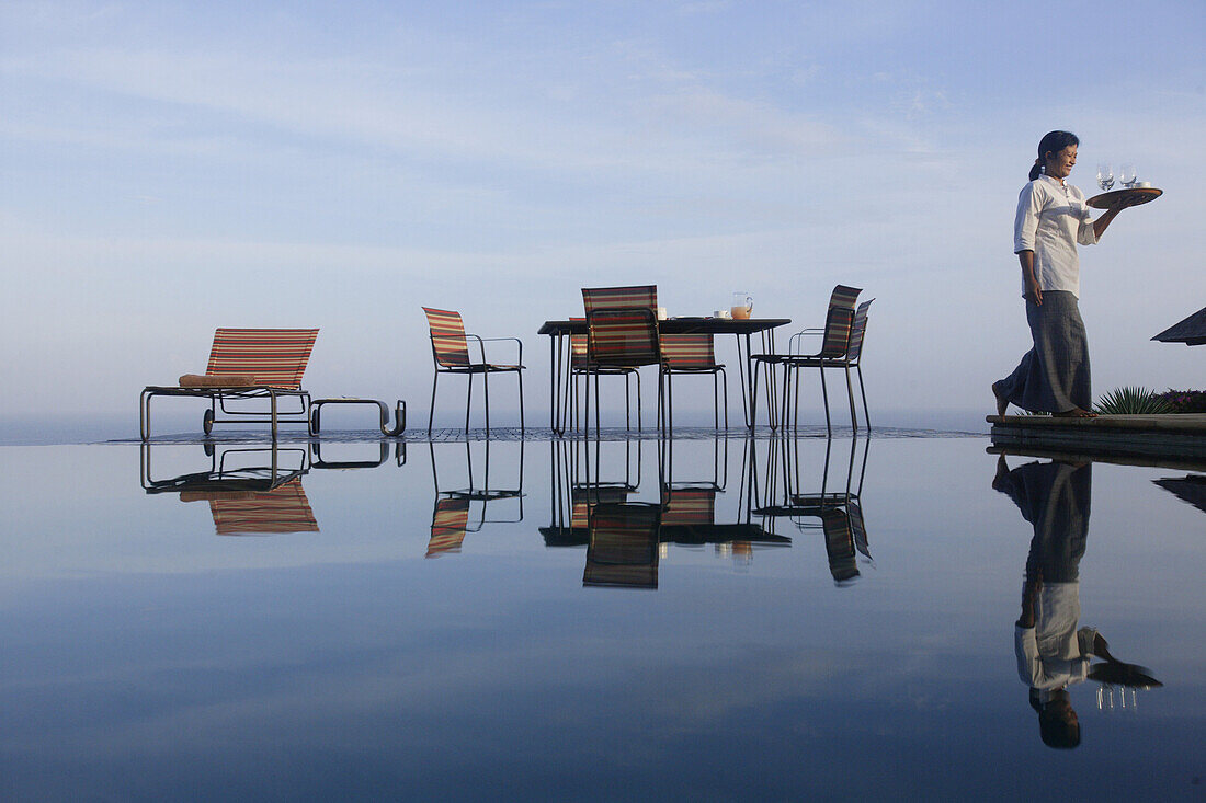 Stühle spiegeln sich auf Wasserfläche, Frau mit Tablett, Bali, Indonesien