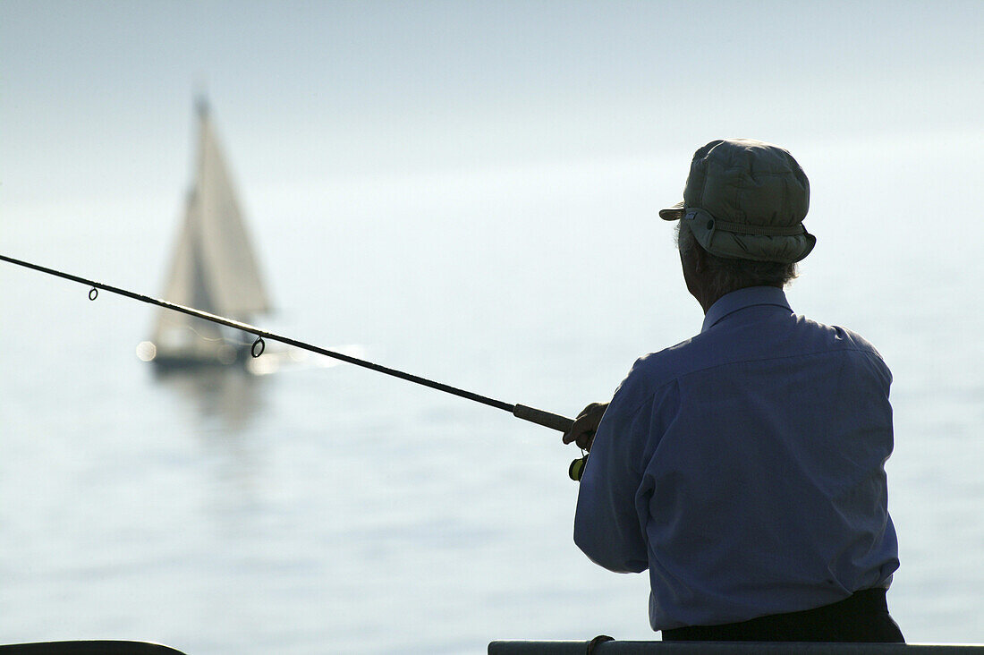 Angler am Bodensee, Segelboot im Hintergrund, Bodensee, Baden-Württemberg, Deutschland