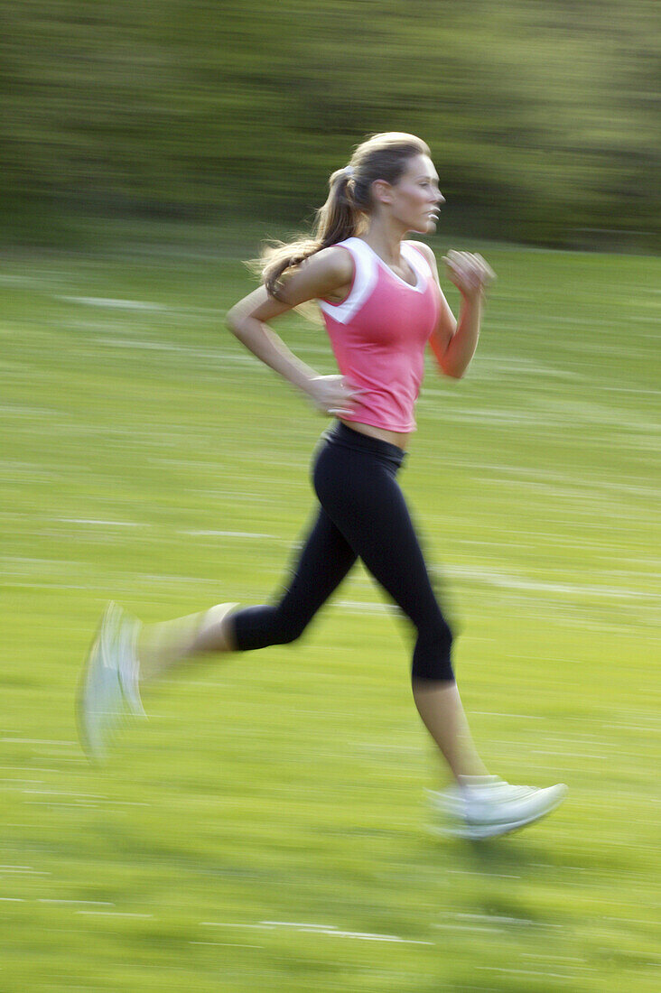 Young woman wearing a pink top, jogging through green fields, Bavaria, Germany