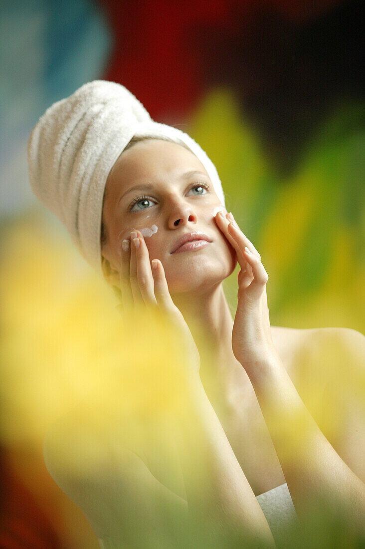 Young woman applying cream onto her face, Beauty