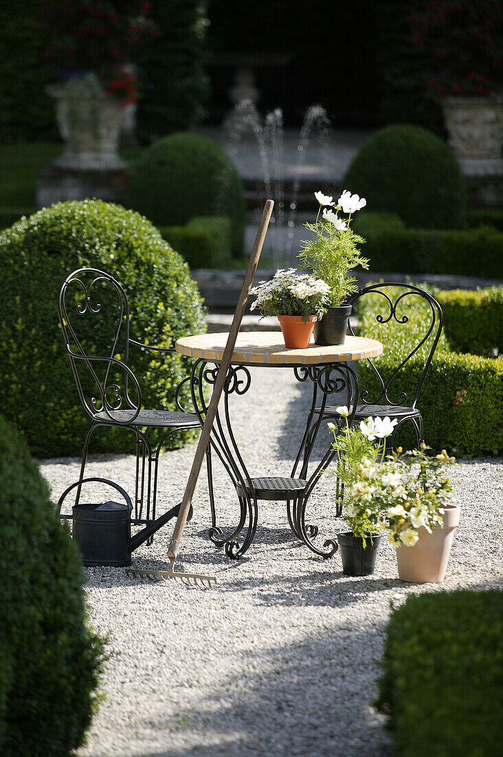 Cultivated garden with wrought iron garden furniture, rake, watering can, Munich, Bavaria, Germany