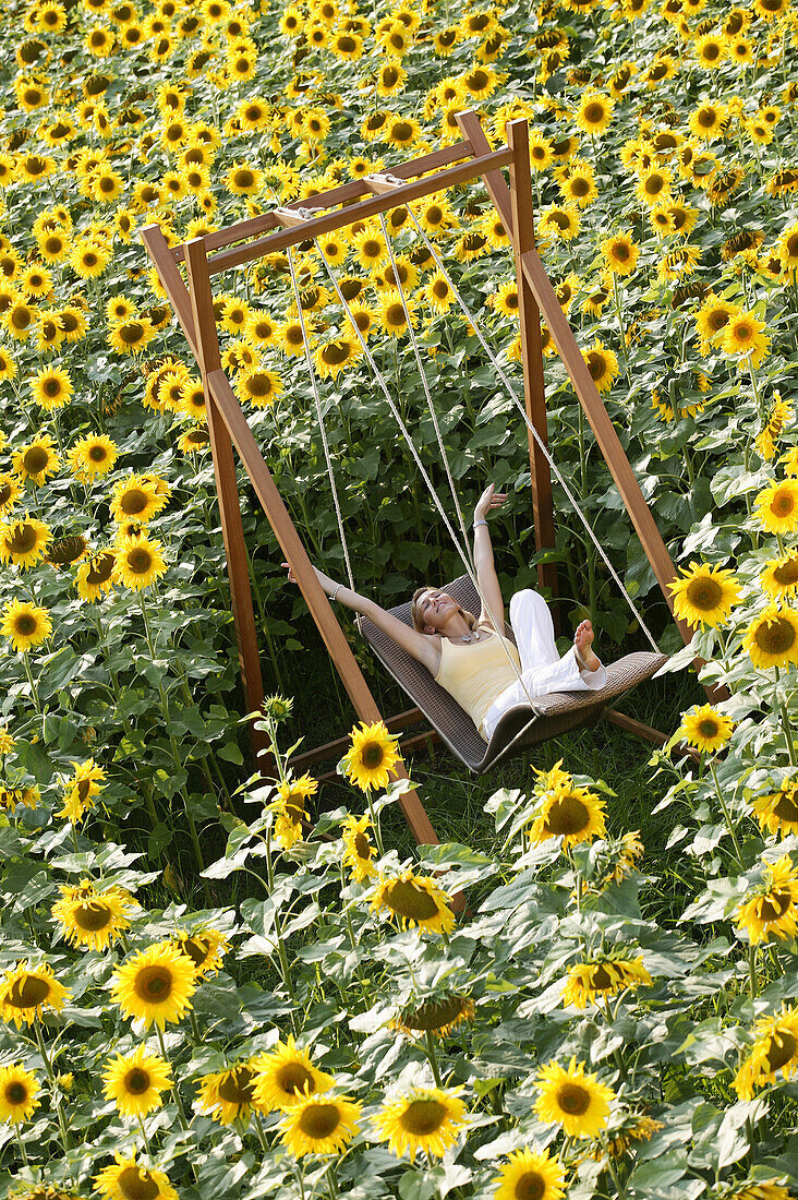 Junge Frau auf Schaukel in Sonnenblumenfeld, Bayern, Deutschland
