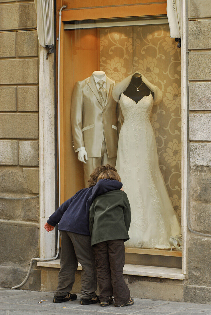 Two children embracing in front of shop window with bride's gown, Grosseto, Tuscany, Italy, Europe