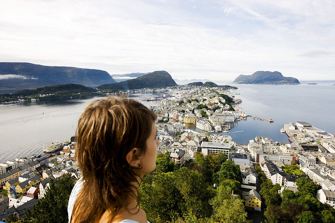 Junge Frau schaut auf die Stadt Alesund unter Wolkenhimmel, More og Romsdal, Norwegen, Skandinavien, Hafenstadt, Europa