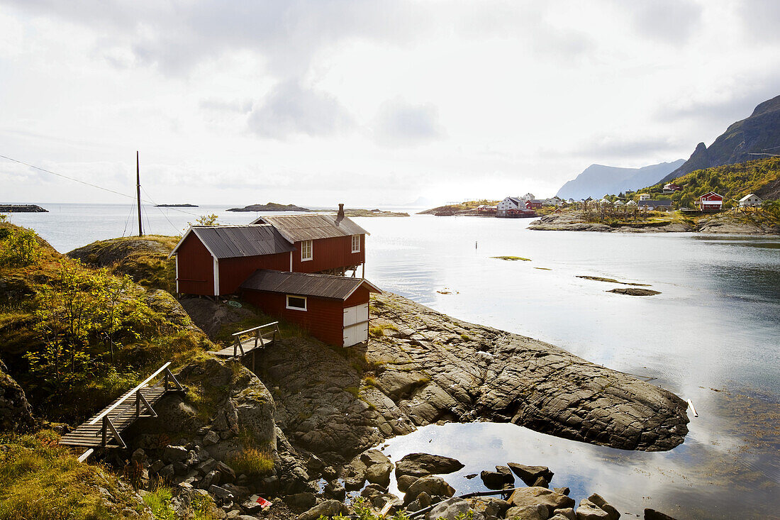 Rote Rorbu Hütte am Wasser in steiniger Küstenlandschaft, Lofoten, Norwegen, Skandinavien; Landschaft, Europa