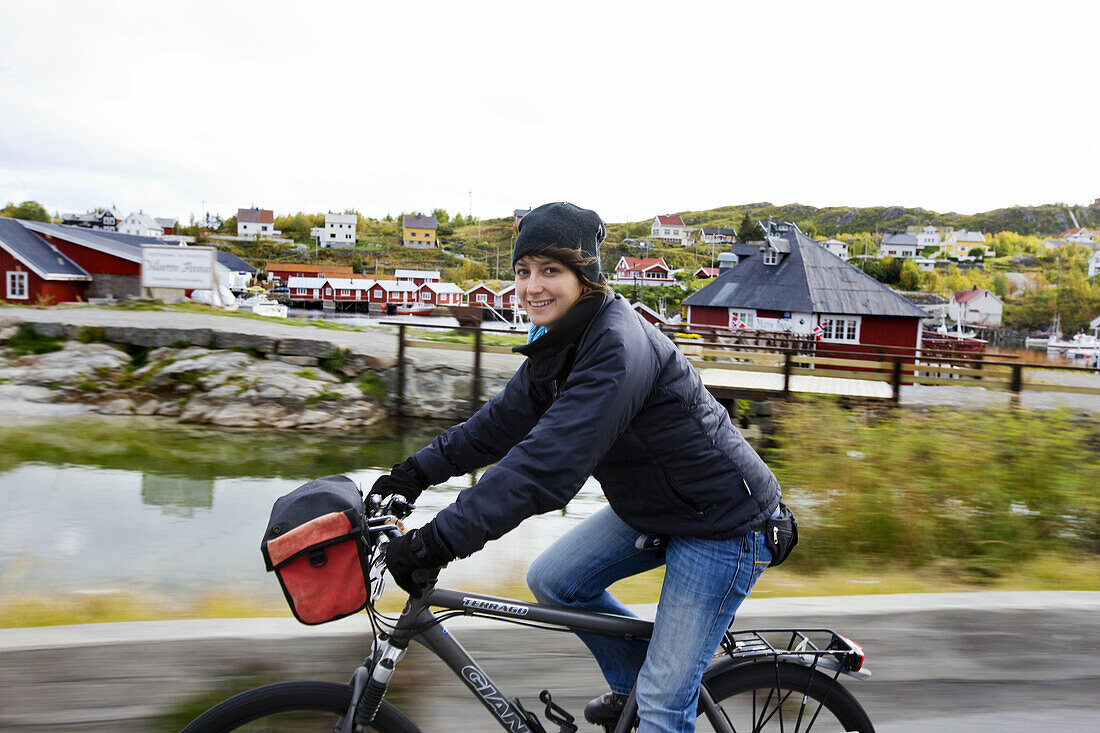 Young woman cycling and smiling in front of Reine, Lofoten, Norway, Scandinavia, Europe