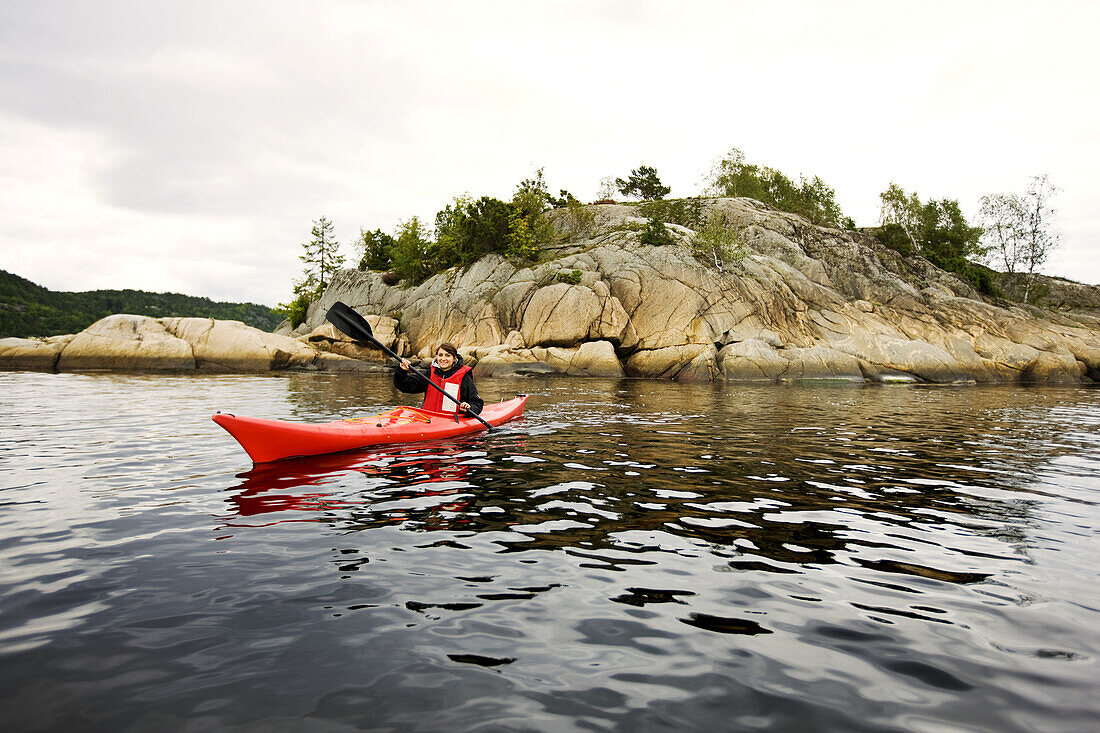 Young woman kayaking at the rocky coastline, Skaggerak, Sorland,  Norway, Scandinavia, Europe