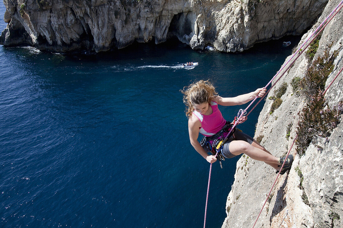 A young woman abseiling from the cliffs at the bay of Zurrieq, Malta, Europe