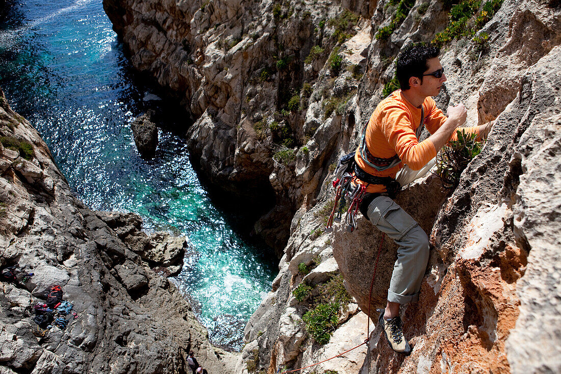 Ein junger Mann, eine Sportkletterer, klettert an den Klippen der Bucht von Zurrieq, Malta, Europa