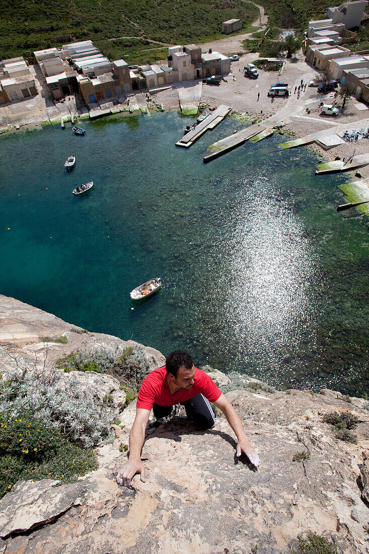 A young man climbing above the Inland Sea in the sunlight, Dwerja Bay, Gozo, Malta, Europe
