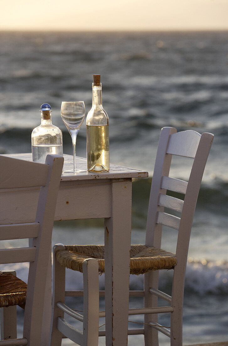 Tisch mit Weinflasche und Weinglas am Meer in der Abenddämmerung, Klein Venedig in Mykonos, Griechenland, Europa