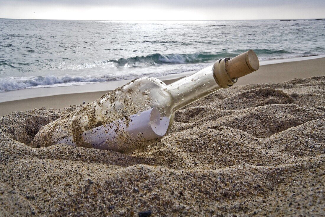 A bottle containing a message lies on a beach at sunset