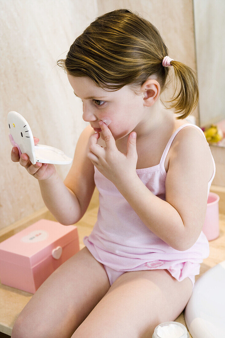 Little girl applying cream on her face