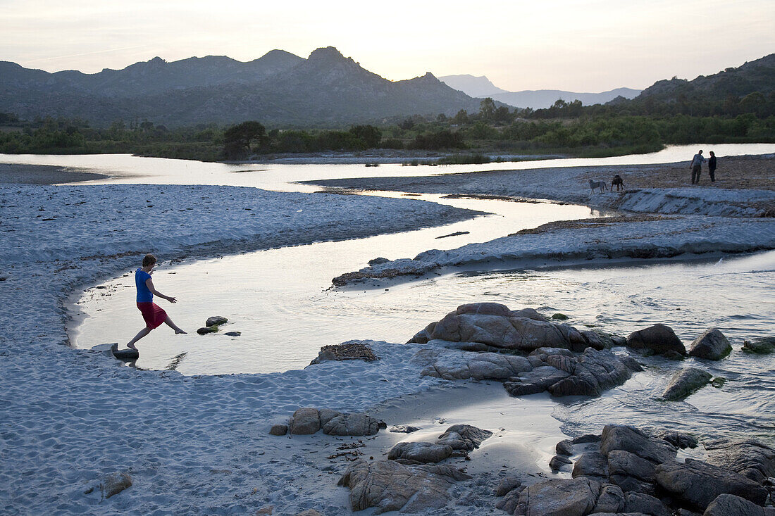 Junge Frau tritt auf Stein im Fluss, Strand von Berchidda im Abendlicht, Fluss fliesst ins Meer, Berchidda, Siniscola, Sardinien, Italien, Europa