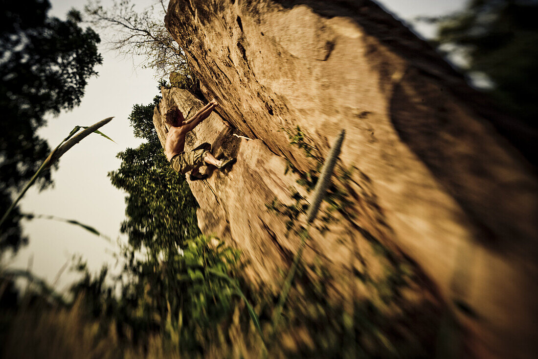 Young man bouldering in the morning sun, Mali, Africa