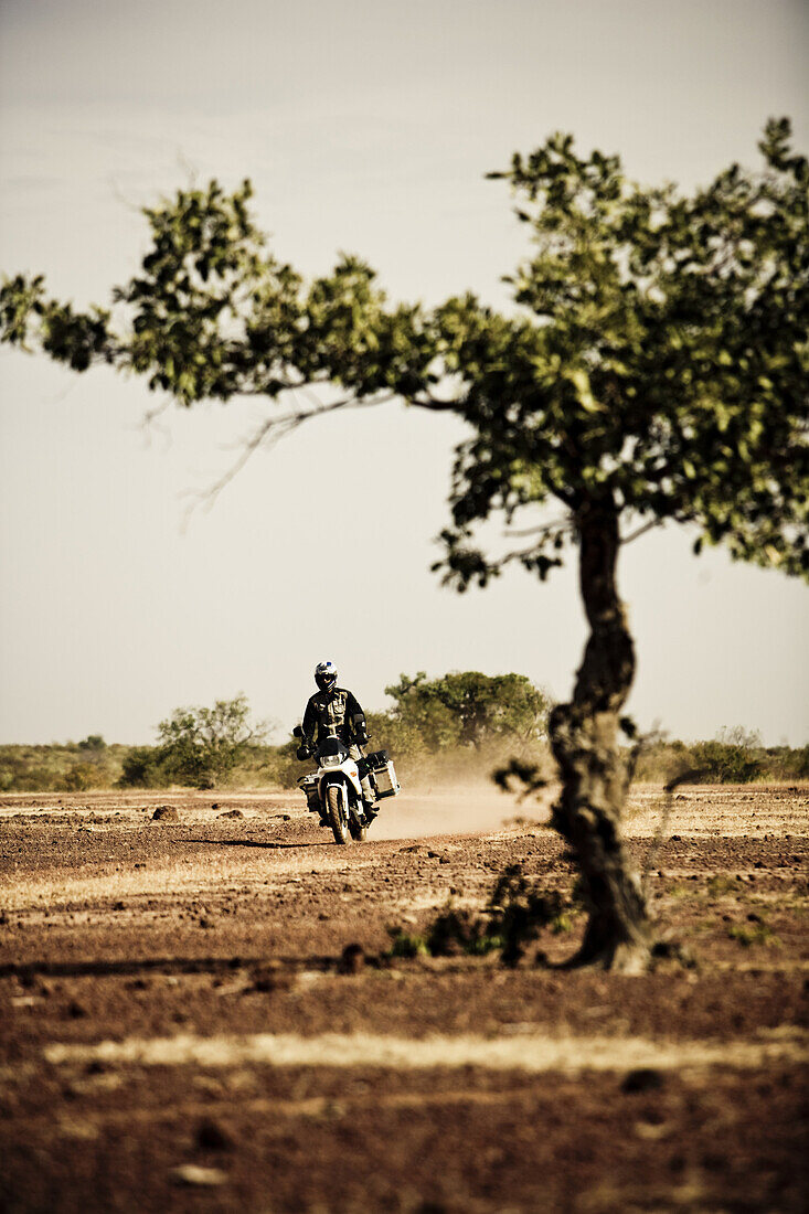 Mann auf Motorrad fährt auf Schotterstrasse durch karge Landschaft, Mali, Afrika