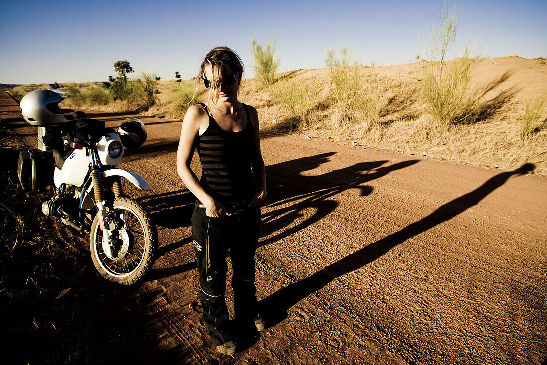 Young woman and motorcycle on dirt road in the evening sun, Mali, Africa