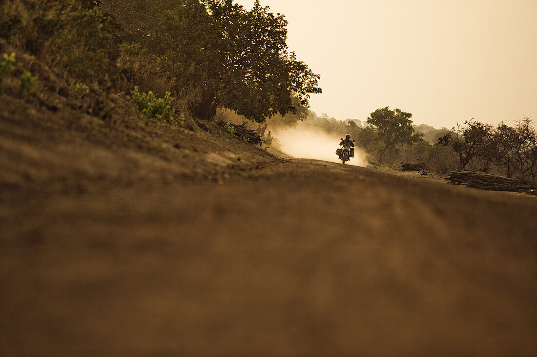 Mann auf Motorrad fährt auf Schotterstrasse am Abend, Mali, Afrika