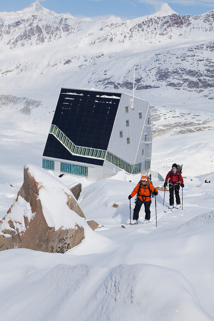 Two female back country skiers, Monte Rosa Hut in background, Canton of Valais, Switzerland